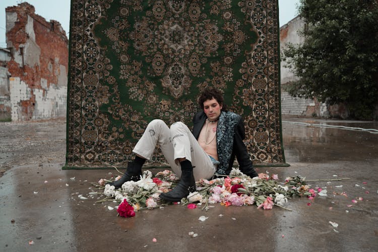 A Man With Unbuttoned Jacket Sitting On Floor With Flowers
