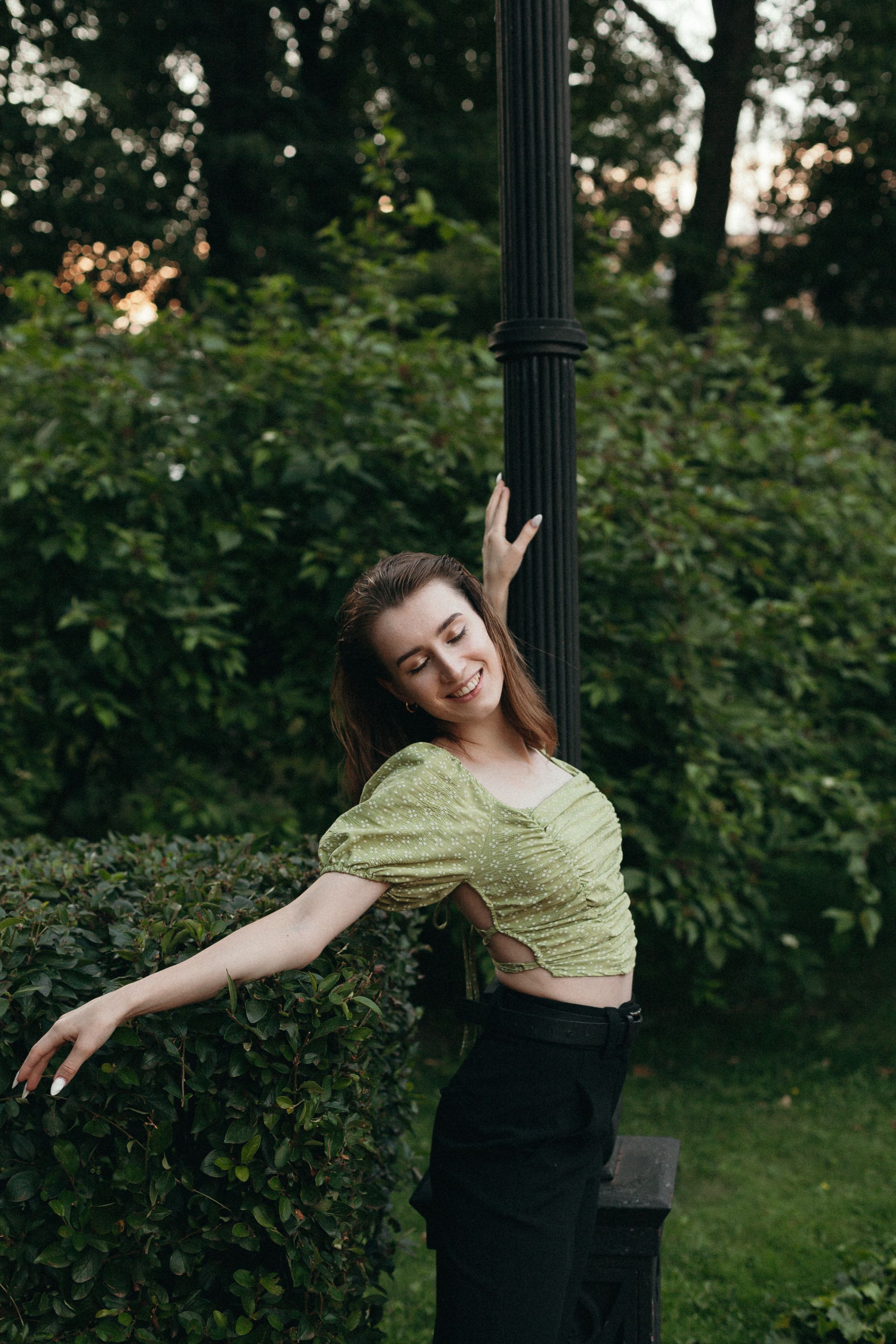Smiling woman in green blouse enjoying nature in a lush park setting.