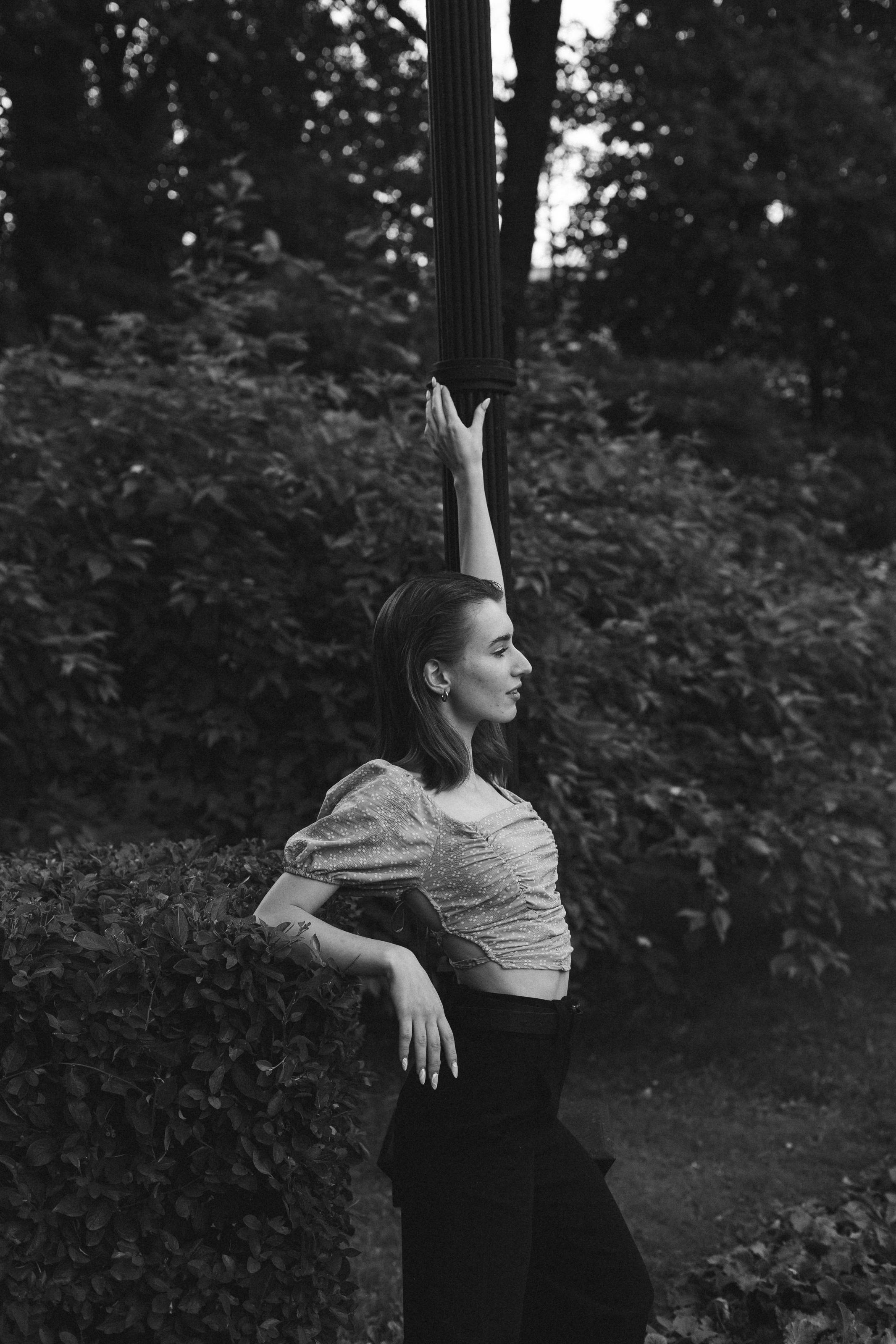 Elegant woman posing by a lamppost in a grayscale outdoor setting.