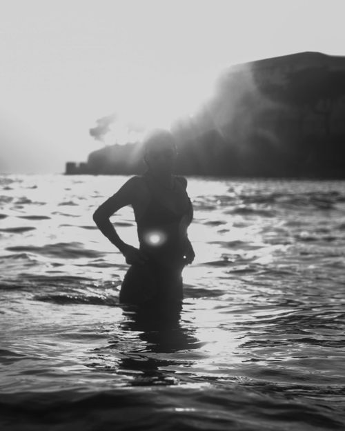 Free Silhouette of a woman wading in the ocean during sunrise, creating a serene beach scene. Stock Photo