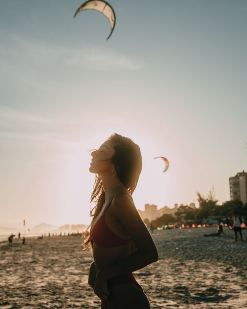 Free Woman enjoying a serene sunset on Ipanema Beach, Rio de Janeiro, with kites in the background. Stock Photo