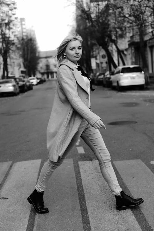 Grayscale Photo of Woman in Coat and Pants Walking on the Street
