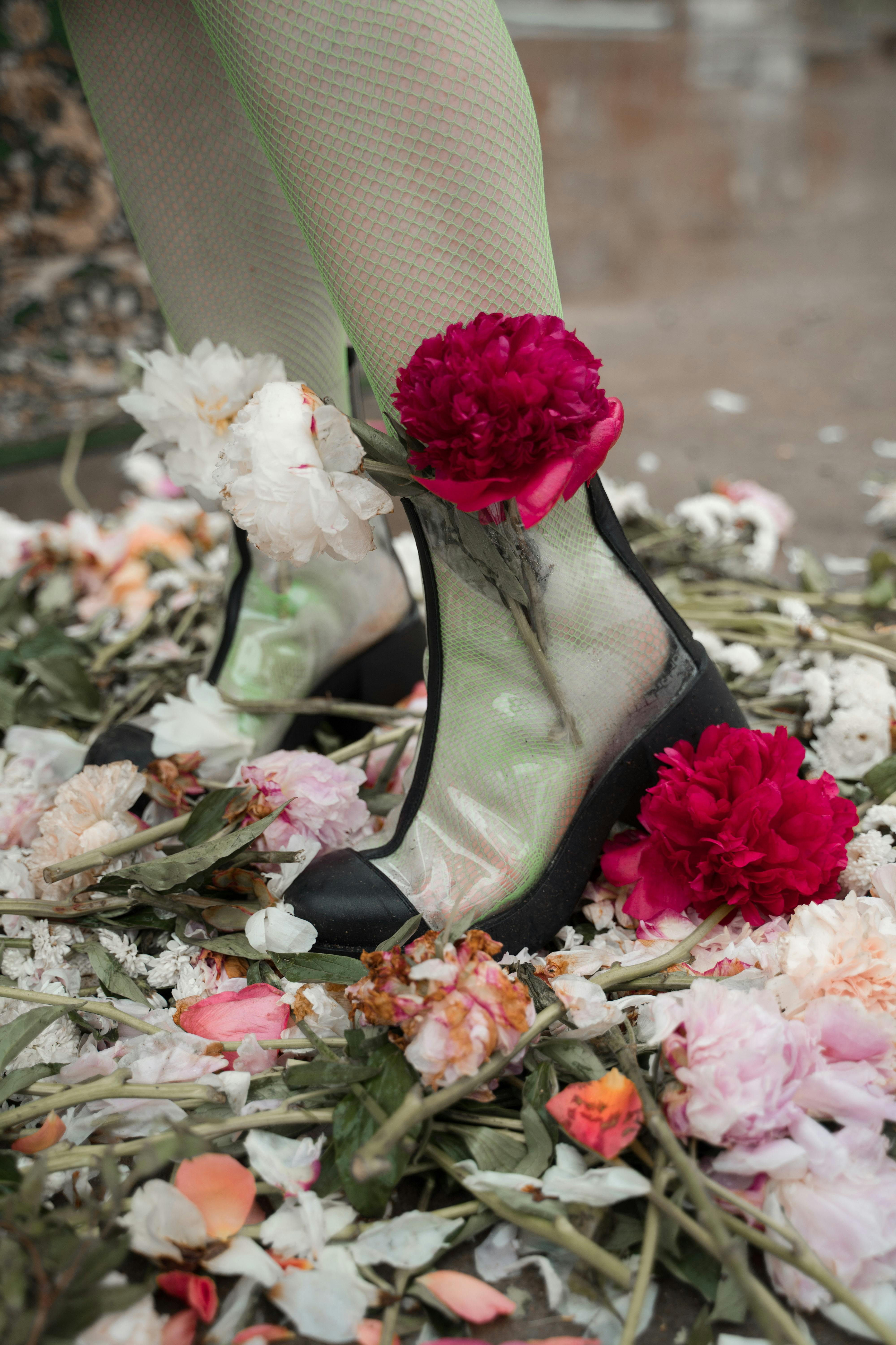 person wearing clear boots and stocking standing on a pile of flowers