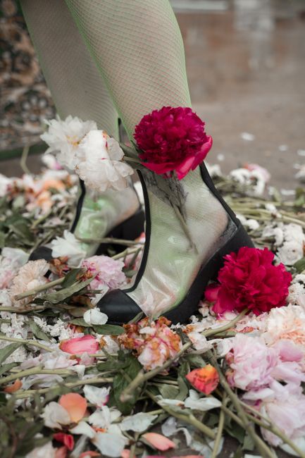 Artistic photo of transparent boots with vibrant flowers amidst scattered blooms.