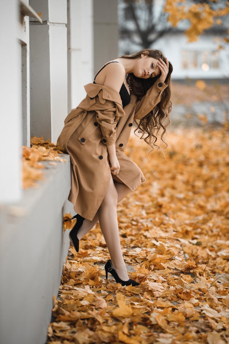 Woman In Coat Ans Stilettos Leaning Against Building And Uncovering Her Shoulder