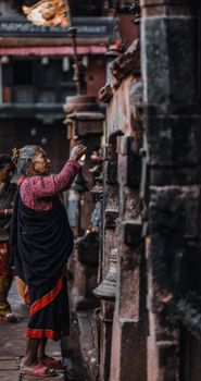 An elderly woman rings traditional temple bells in Dhaka, capturing cultural spirituality.