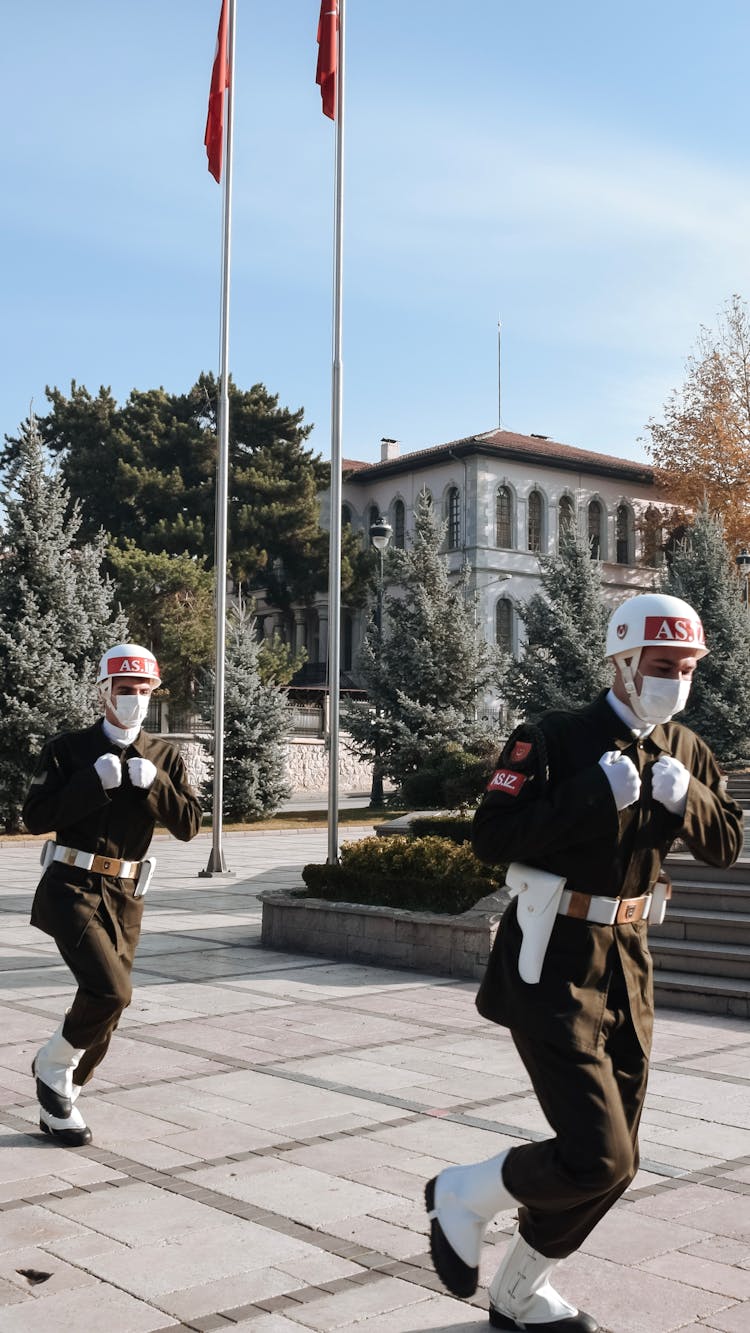 Two Men In Military Uniform Running On The Street While Wearing Face Mask