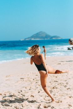 Woman in swimwear playing soccer on sandy beach with ocean view.