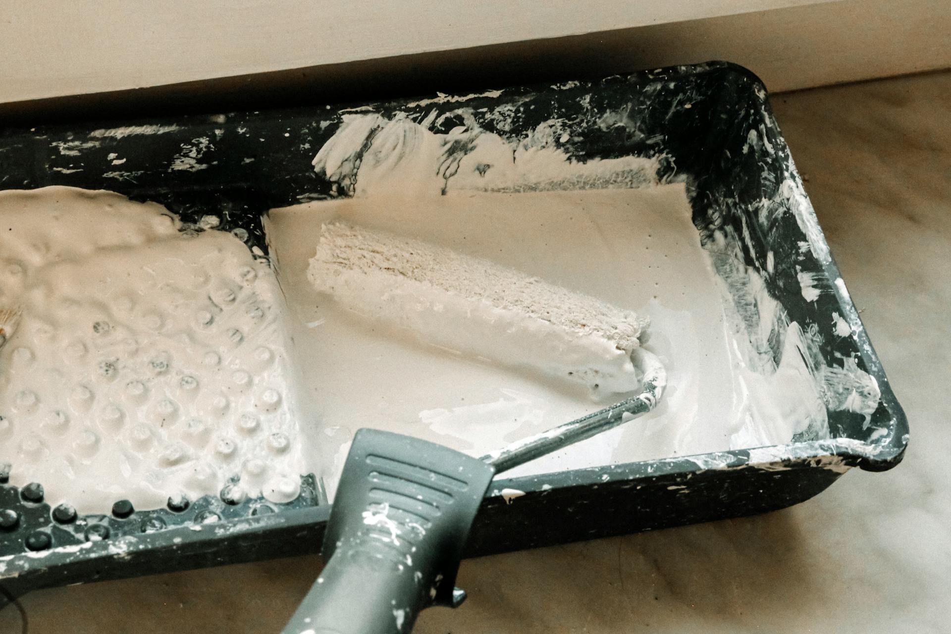 A paint roller dipped in white paint in a plastic tray, ideal for home renovation projects.