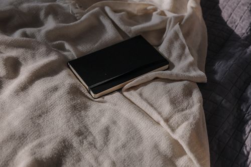Free A black notebook rests on a beige blanket, capturing a minimalist and cozy vibe. Stock Photo
