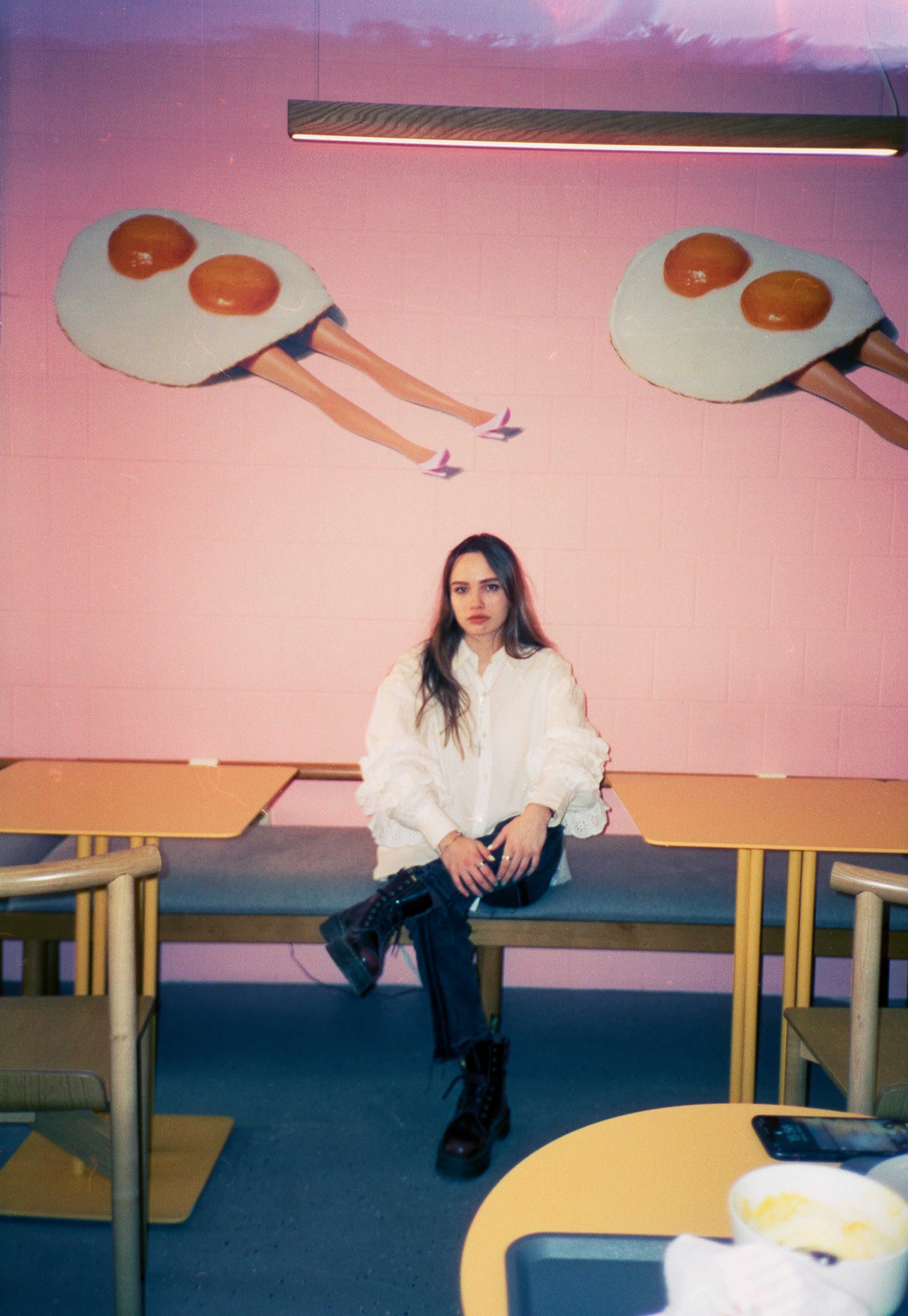 A fashionable woman sits in a colorful modern canteen with creative wall art.