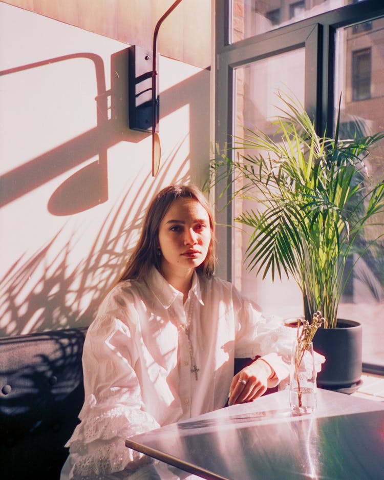 Sad Teenage Girl Sitting At Table By Window In Sunlight At Dawn