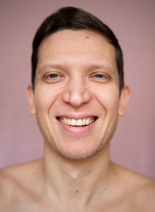 Free Close-up portrait of a smiling shirtless man against a soft pink background. Stock Photo