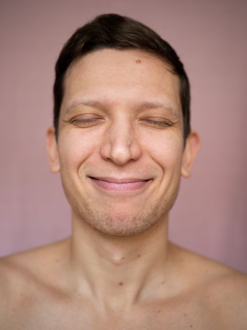 Free A happy young man smiling with eyes closed against a pink background. Stock Photo