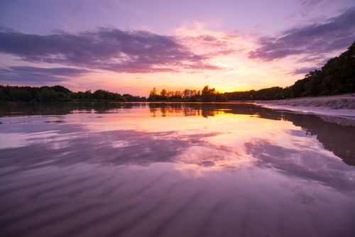 Free Peaceful beach scene at sunset with colorful sky reflecting on the calm water. Stock Photo