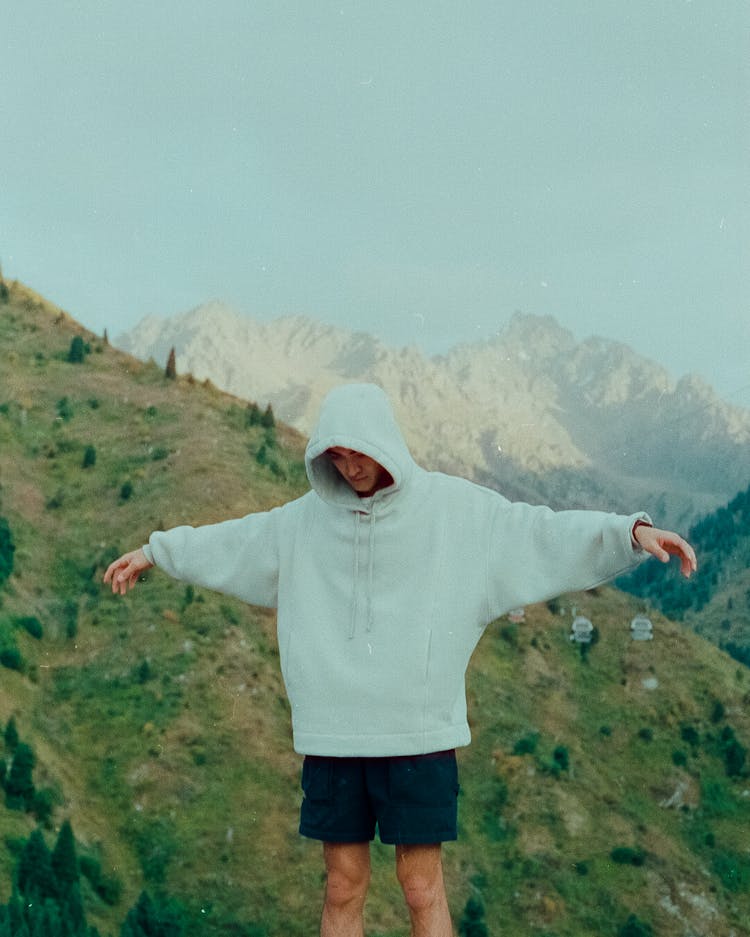 Young Hooded Guy Standing With Outstretched Arms In Mountains