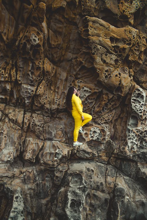 A Woman in Yellow Long Sleeves Shirt and Pants Standing on a Rock Formation