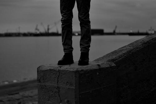 Person in Black Pants and Black Boots Standing on Concrete Barrier