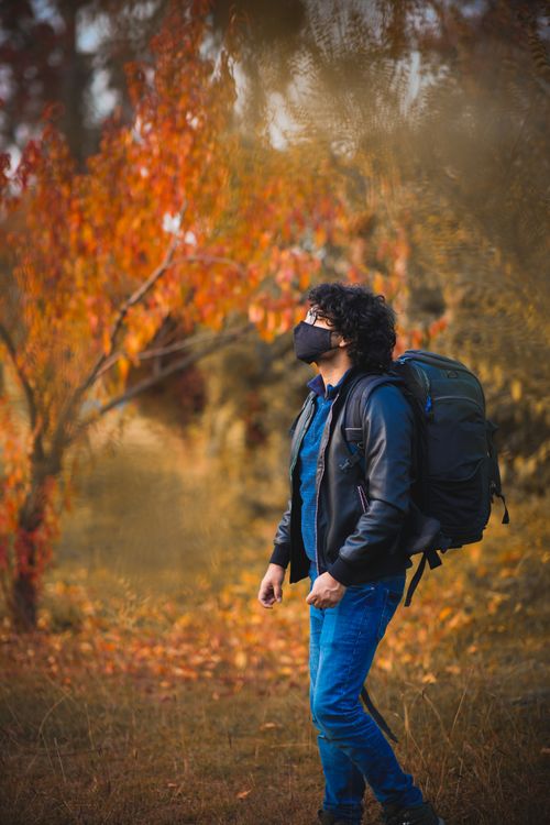 Free Adult man in black jacket hiking in autumn park, wearing a face mask for safety. Stock Photo