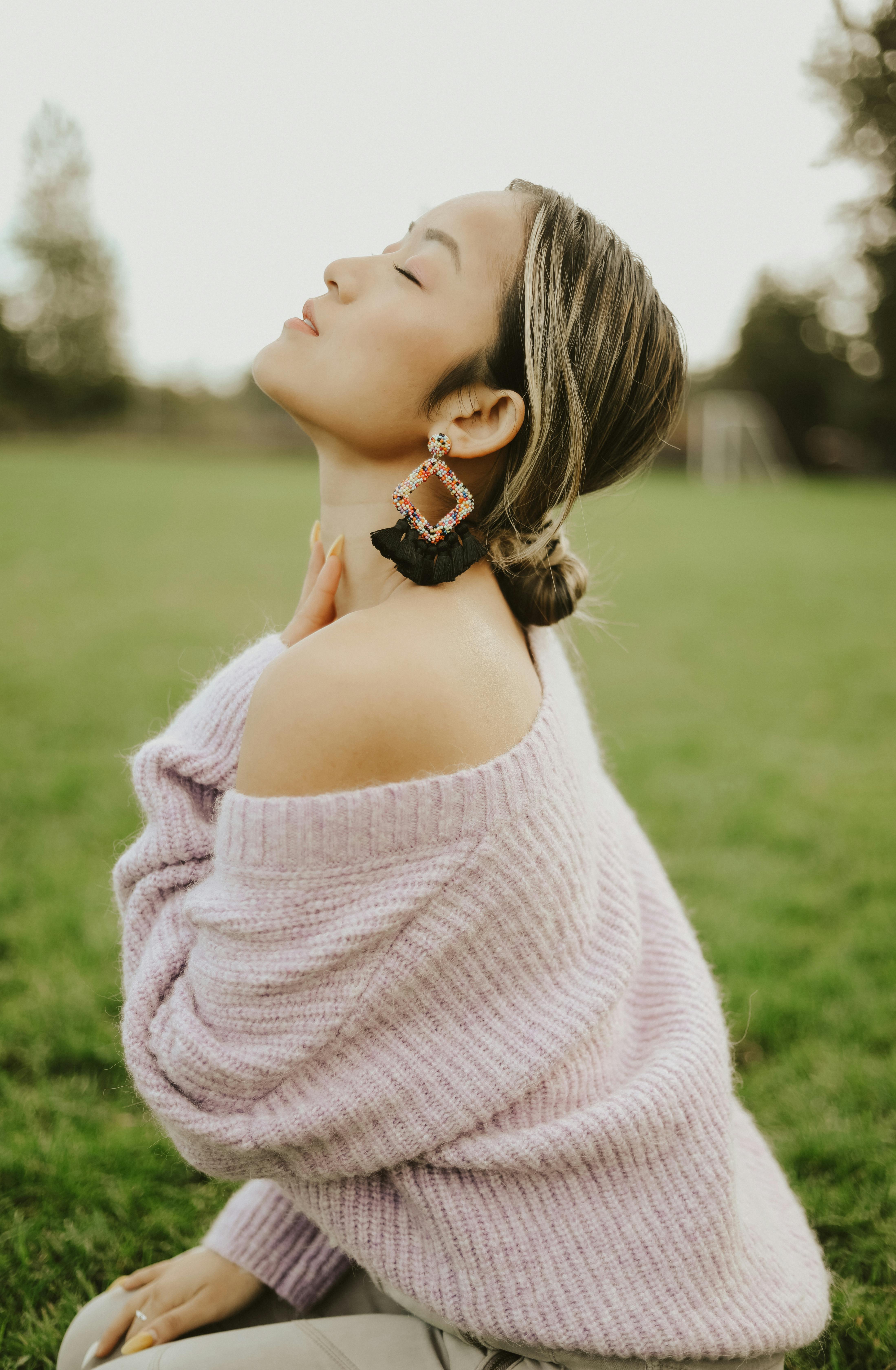 Elegant woman in pink sweater with eyes closed, posing outdoors, showcasing chic fashion style.