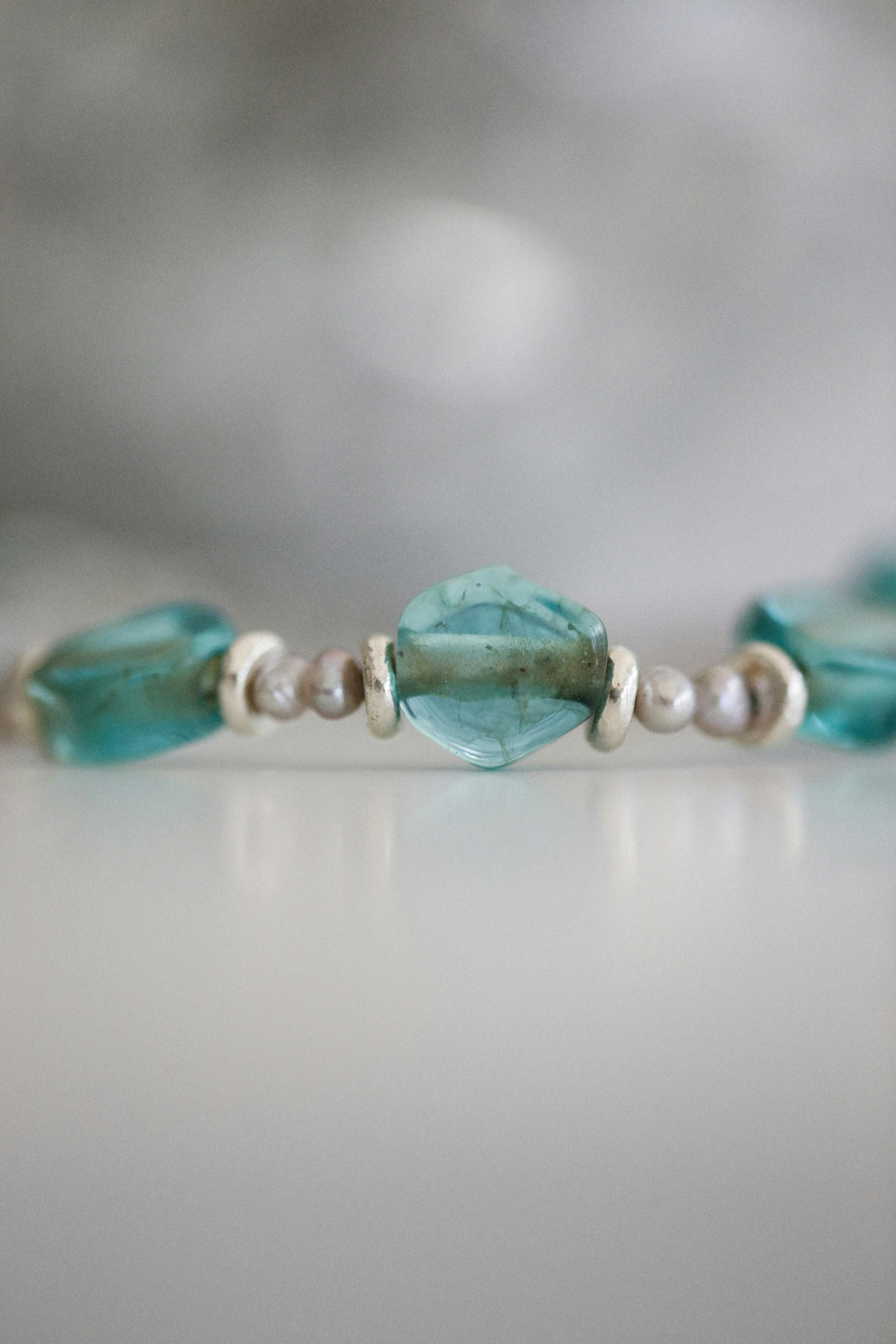 Alexey Demidov - Close-up of a beaded bracelet with turquoise gems on a gray background.
