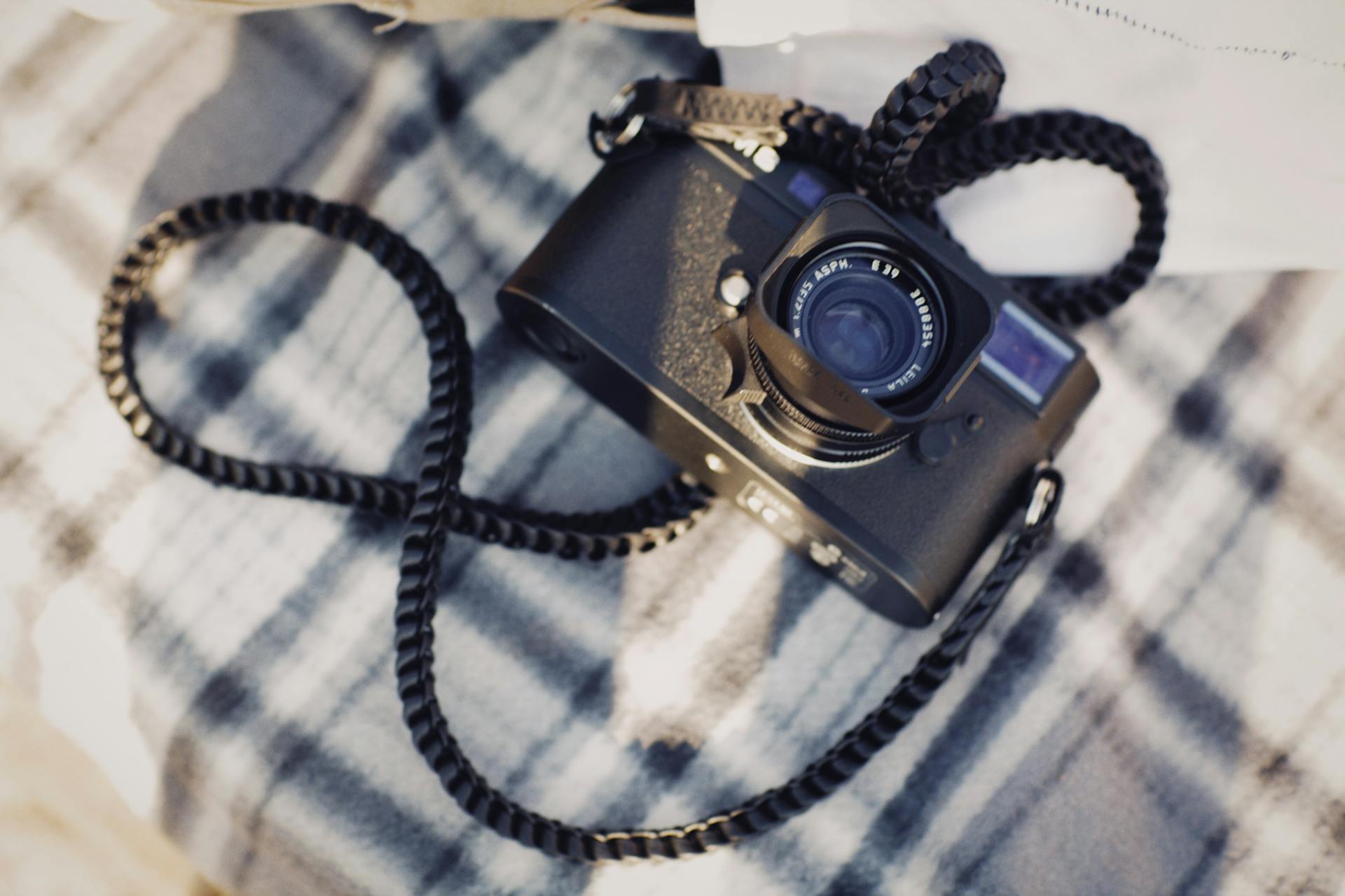 A close-up of a vintage camera with a woven strap on a plaid blanket.