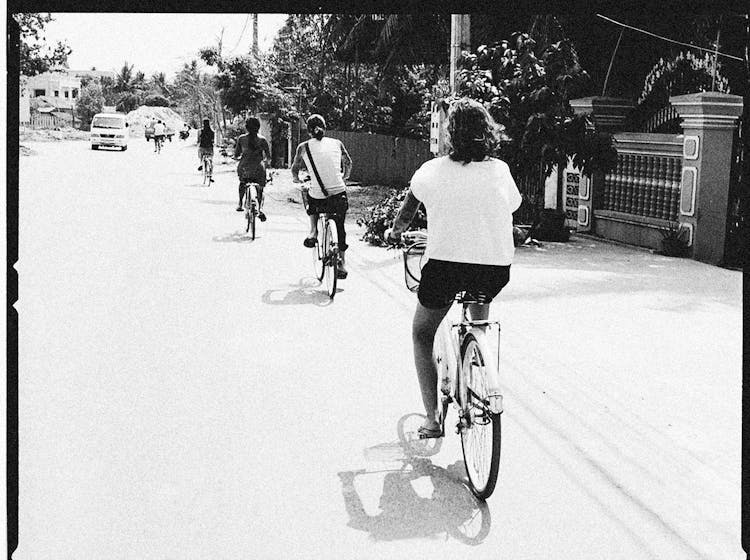 A Grayscale Photo Of People Riding A Bike On The Street