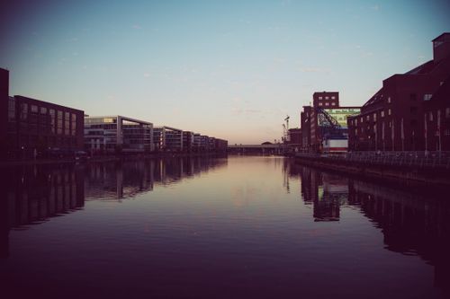 Free A tranquil urban riverfront scene at twilight with reflections and silhouetted buildings. Stock Photo
