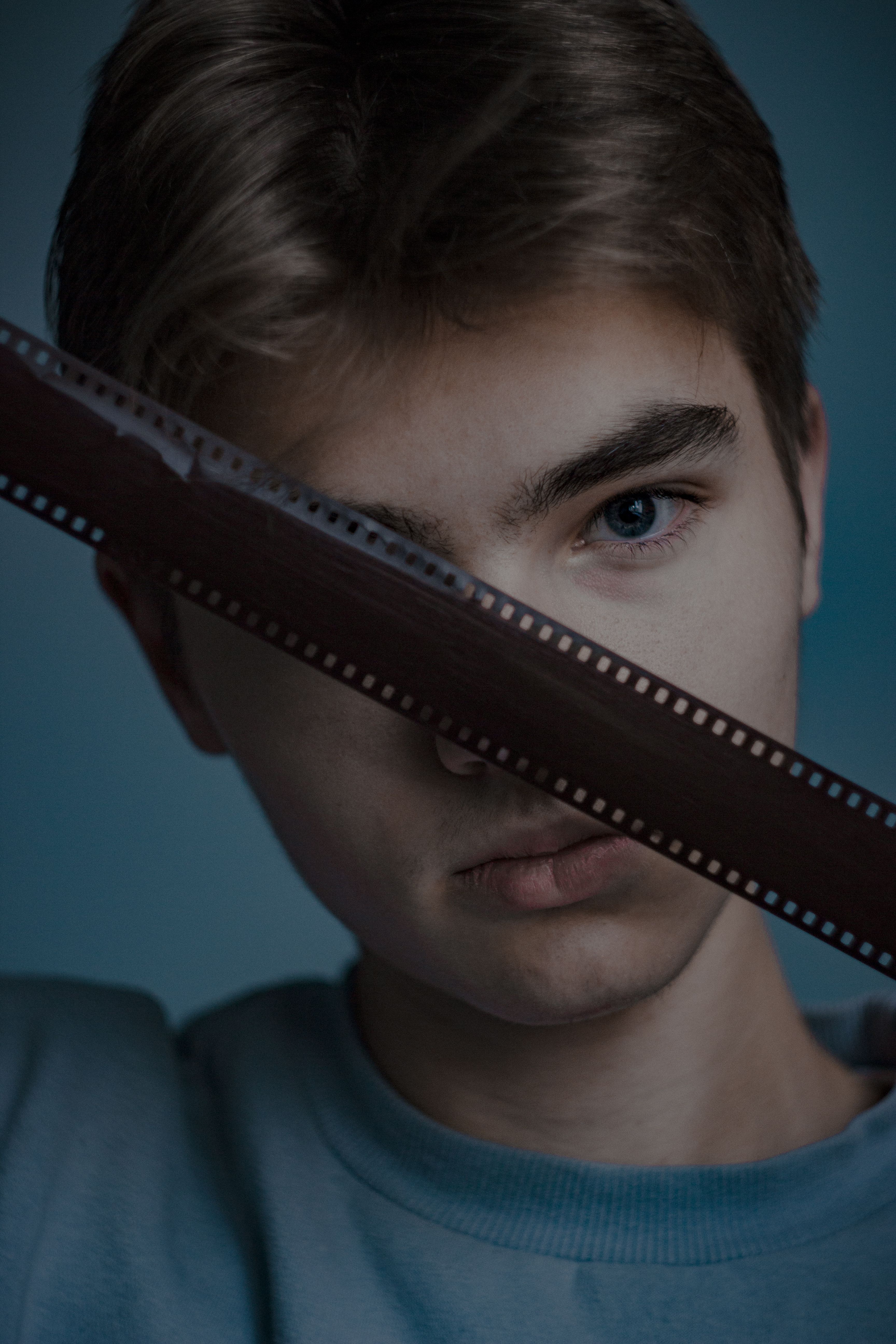 Adolescente posa com uma tira de filme de câmara sobre um fundo azul, mostrando expressão e criatividade.