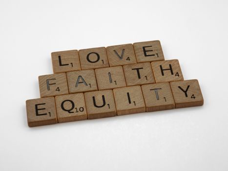 Close-up of wooden Scrabble tiles spelling Love, Faith, and Equity on a white surface.
