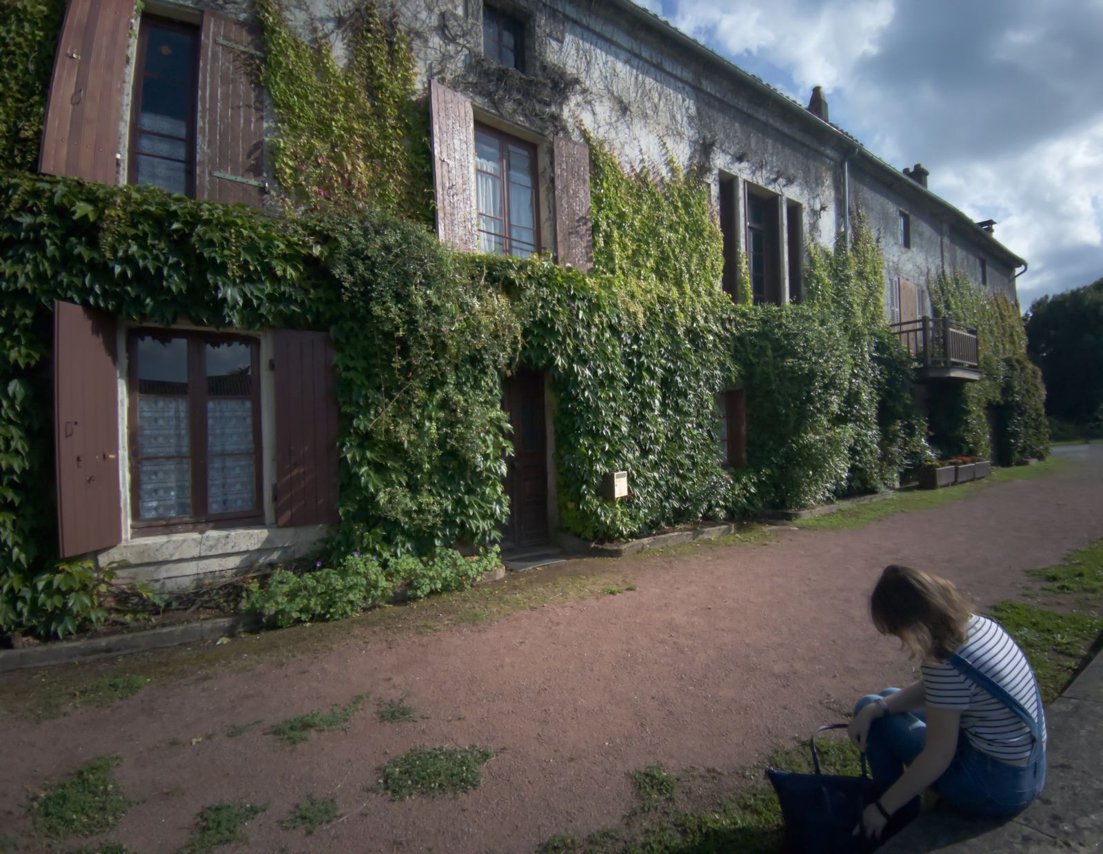Vieille maison couverte de lierre aux volets de bois et femme assise devant