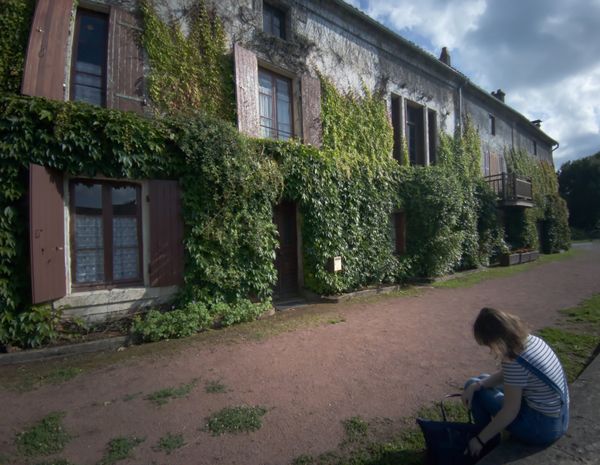 Vieille maison couverte de lierre aux volets de bois et femme assise devant