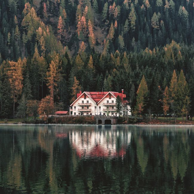 Serene lakehouse amidst dense autumn forest reflecting in calm waters.