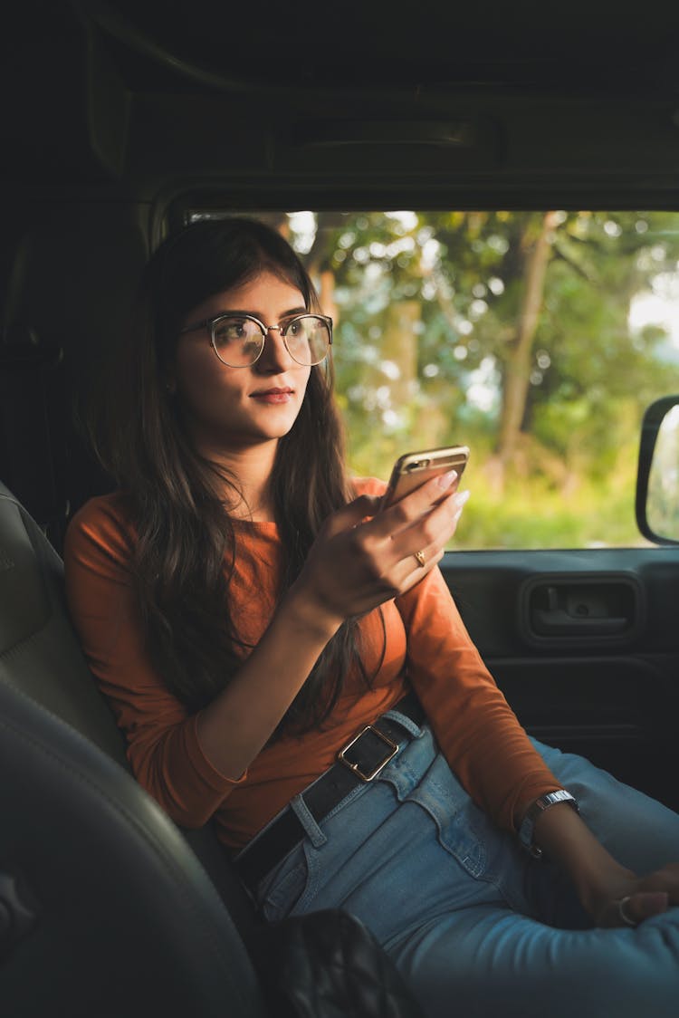 Woman In Orange Long Sleeve Shirt Sitting Inside The Car While Texting