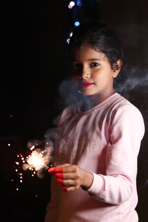 Free A young girl joyfully holds a sparkler against a nighttime backdrop, creating a festive and magical mood. Stock Photo