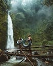 Two Person Carrying Black Inflatable Pool Float on Brown Wooden Bridge Near Waterfalls