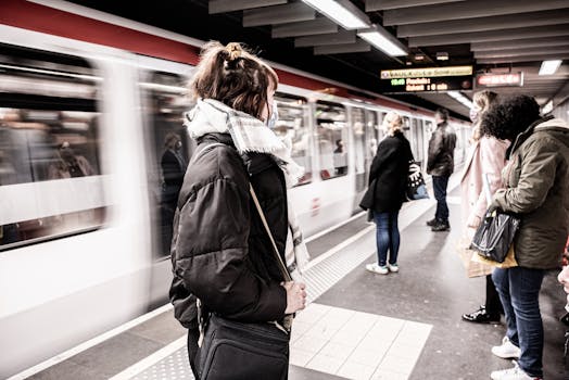 Commuters wait on a subway platform in France with a train passing by.