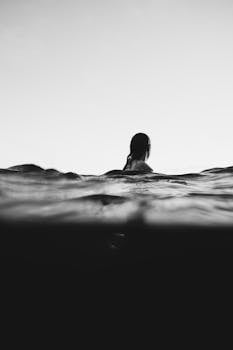 一张黑白艺术照片中，一名女子在黄昏时分游泳，营造出宁静而冒险的氛围