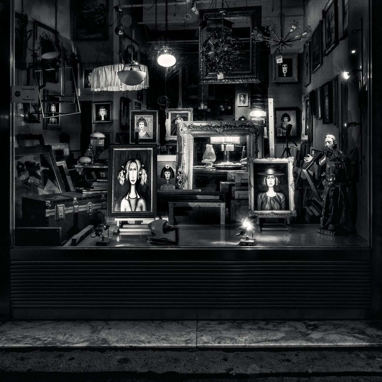 Monochrome view of an art-filled storefront in Vienna displaying framed portraits and sculptures.