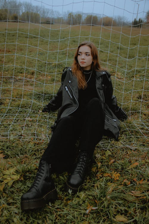 Woman in Black Jacket and Black Pants Sitting on Green Grass