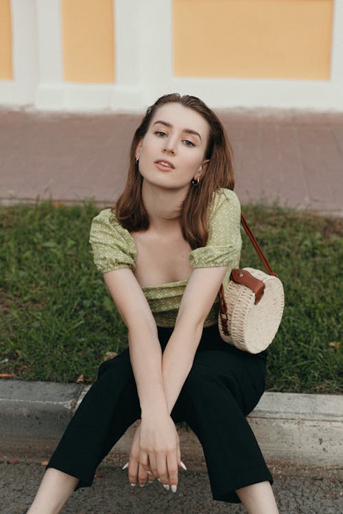 Woman in Green Shirt and Black Pants Sitting beside the Sidewalk