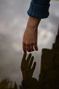 Close-up of a hand reaching towards its reflection on a water surface, creating a serene and contemplative scene.