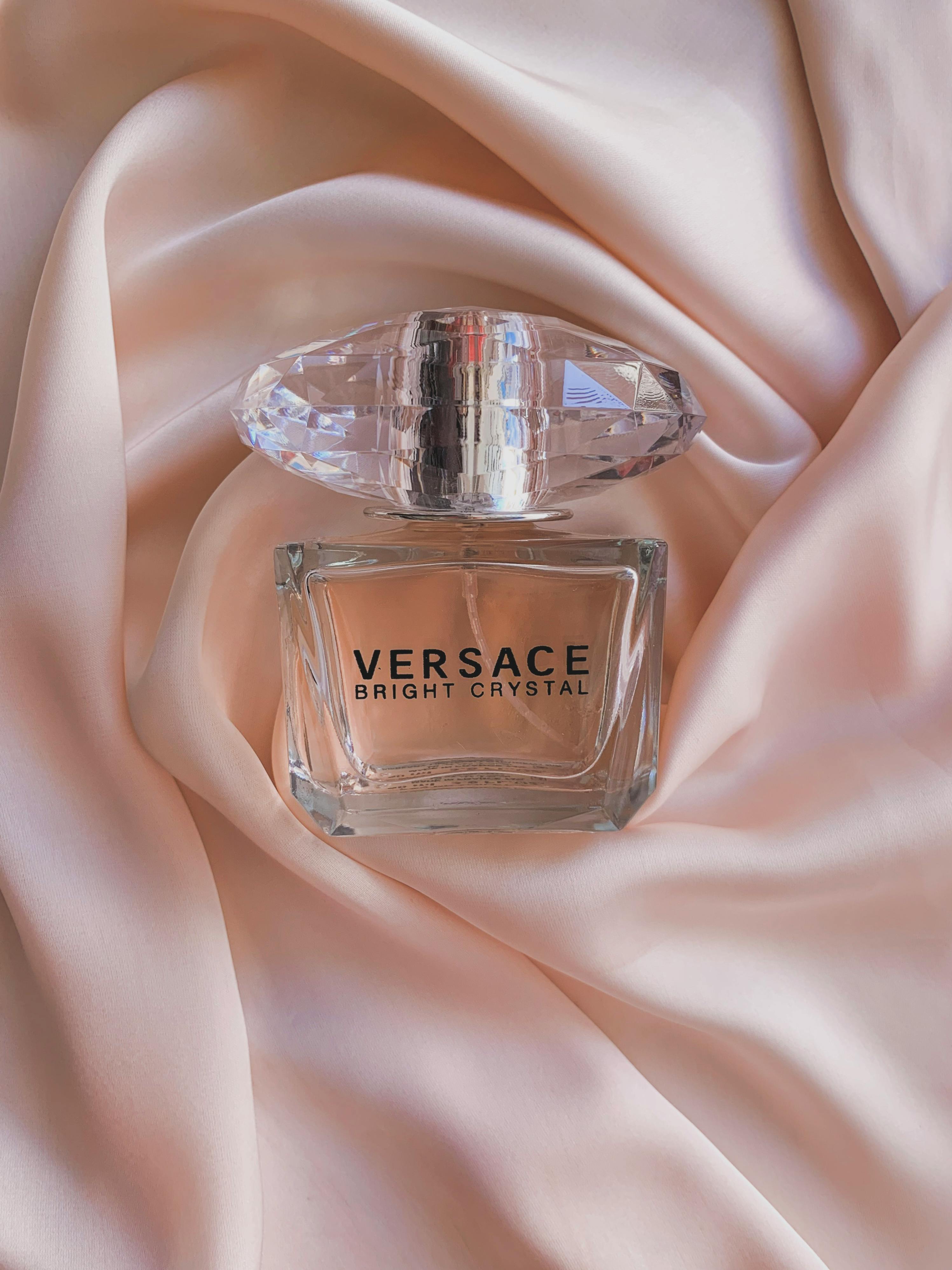 A Versace Bright Crystal perfume bottle elegantly placed on soft pink silk fabric, showcasing luxury.