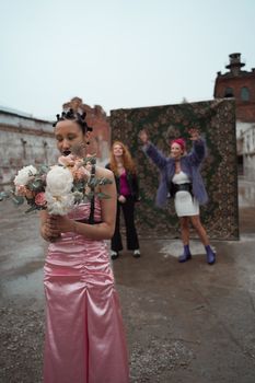 Three women in an urban setting, one holding a bouquet, embodying modern fashion vibes.