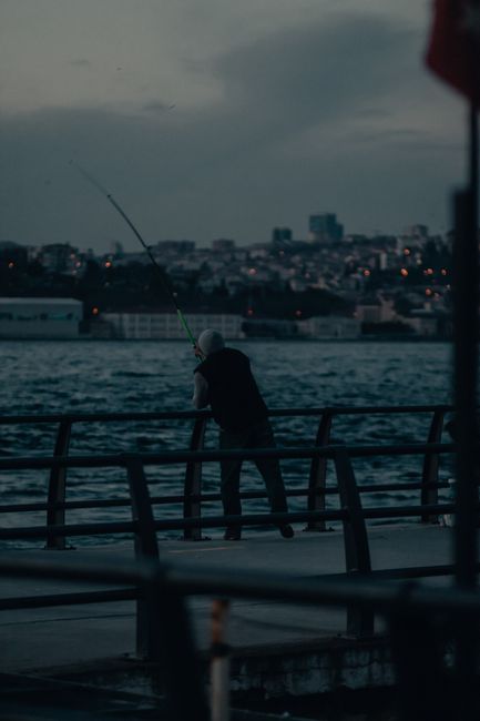 Person fishing by the waterfront in İstanbul at twilight, scenic city backdrop.