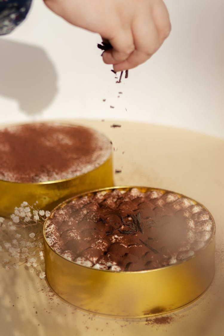 Person Sprinkling Chocolate Flakes On Top Of Cake 