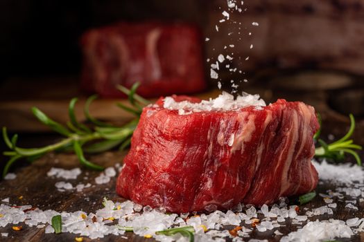 Close-up of raw beef steak with sea salt and herbs on a wooden surface.