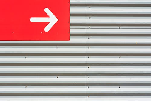 A Red and White Arrow Sign on a Corrugated Steel Wall