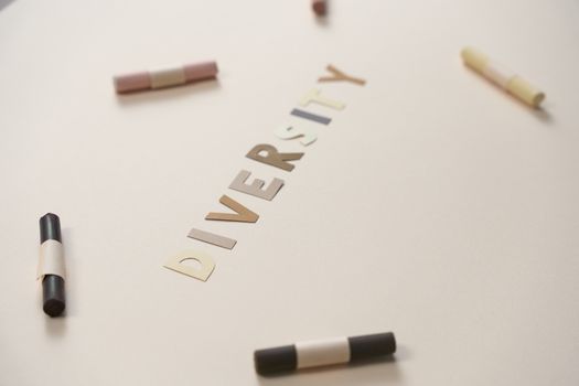 A close-up of colored crayons surrounding cut-out letters spelling 'diversity' on a white background.