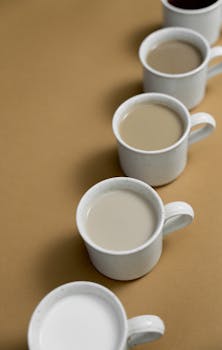 Five ceramic mugs with different coffee and milk gradients on a brown surface in a vertical arrangement.
